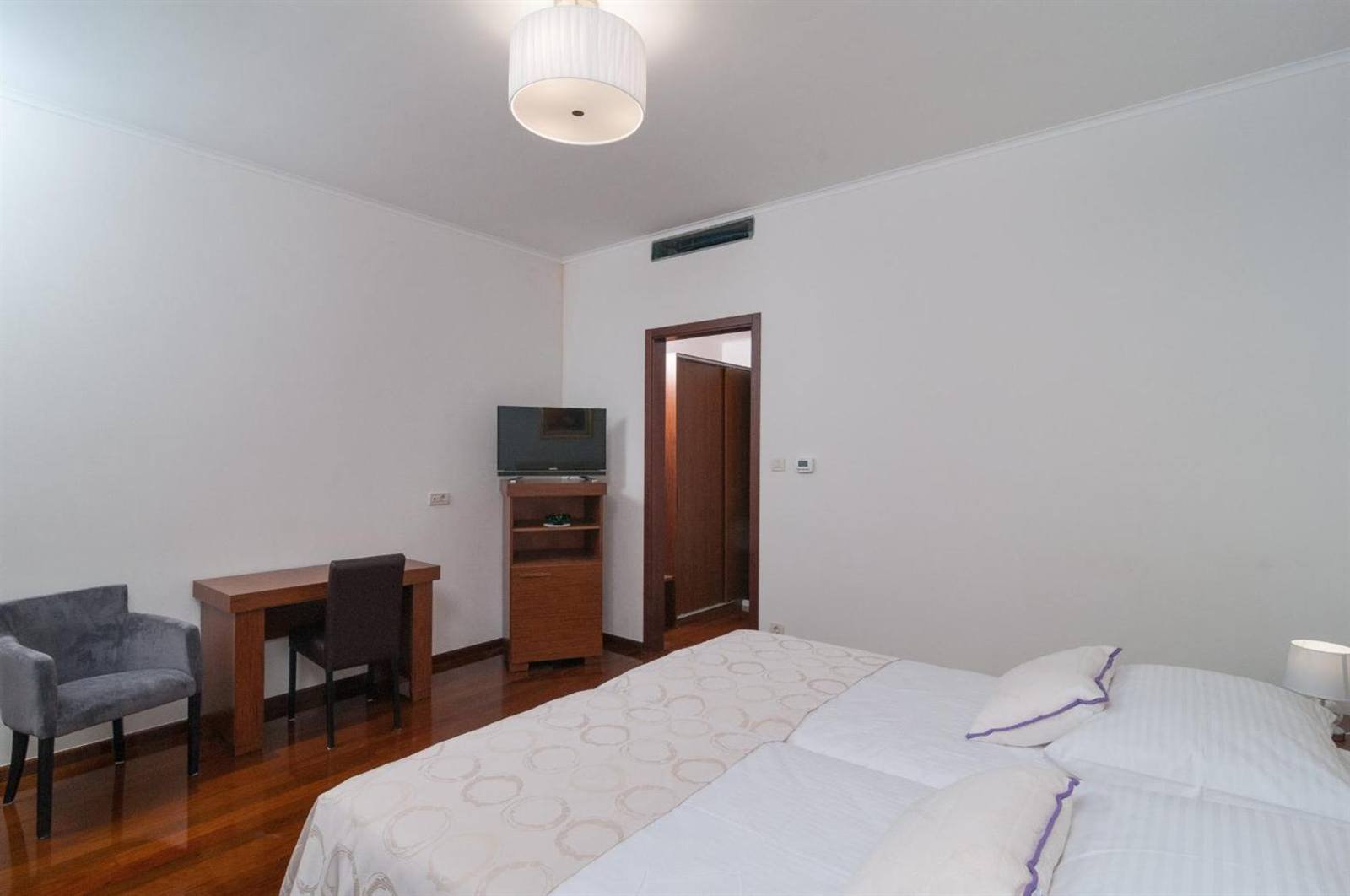 Bright white room with a double bed, desk and armchair